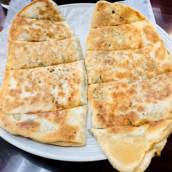 Two golden-brown Afghan flatbreads, sliced into strips, served on a white plate.