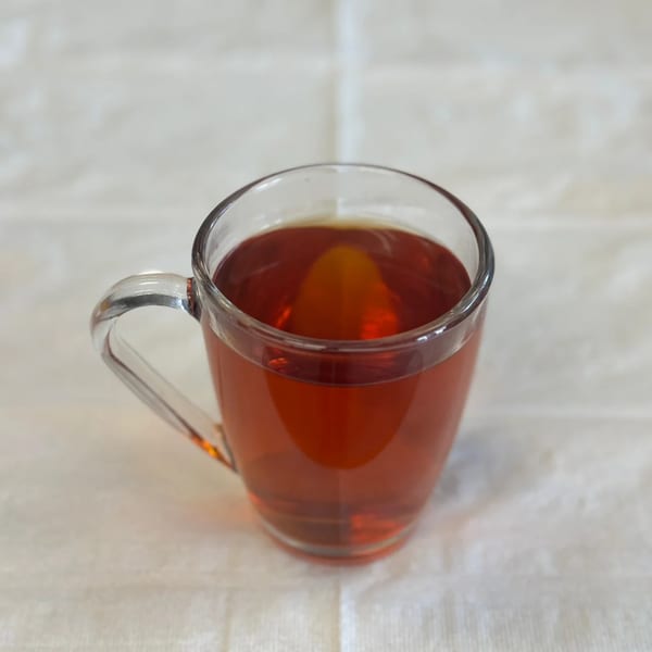 A clear glass mug filled with amber-colored Afghan tea sits on a white tablecloth.