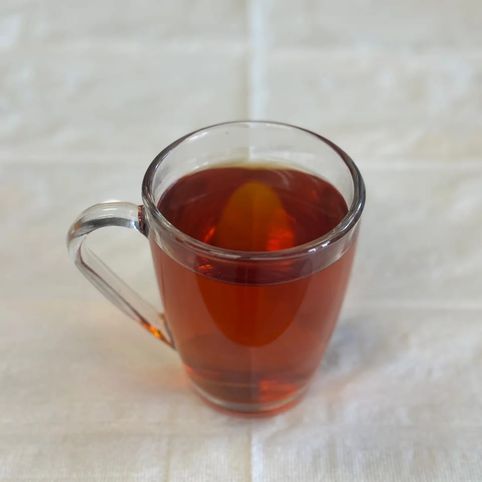 A clear glass mug filled with amber-colored Afghan tea sits on a white tablecloth.