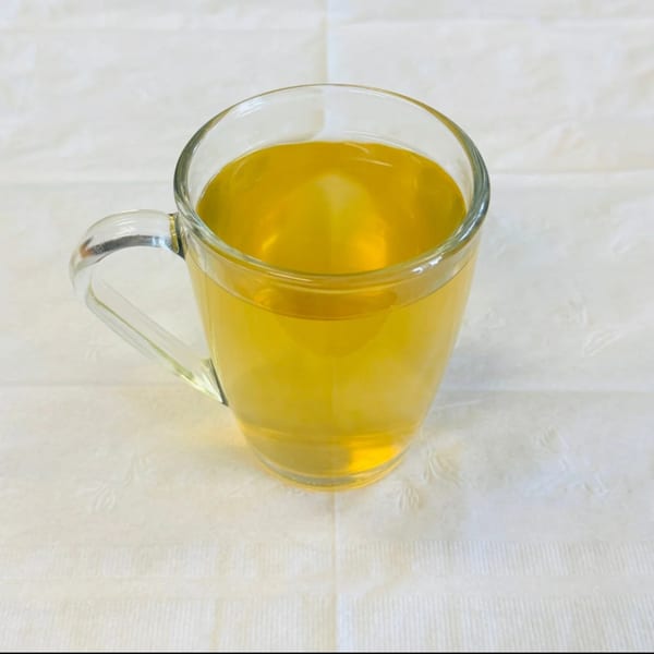 A clear glass mug filled with golden Afghan green tea sits on a white textured tablecloth.