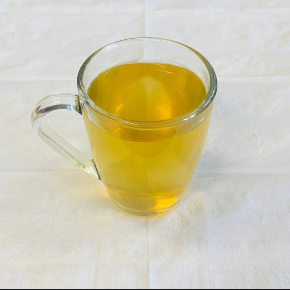 A clear glass mug filled with golden Afghan green tea sits on a white textured tablecloth.