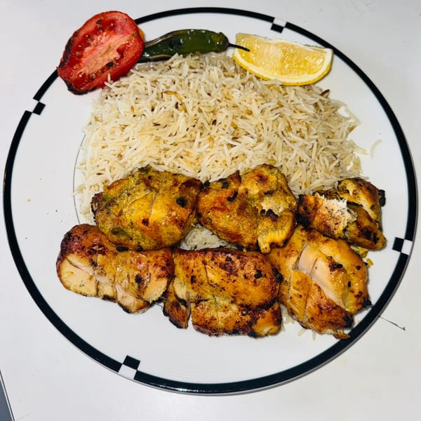 Afghan chicken kabob with rice, grilled tomato, green chili, and a lemon wedge.