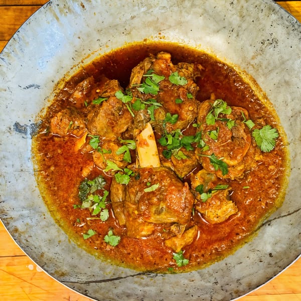 Afghan Kabob House's lamb shank curry, garnished with fresh cilantro, served in a metal dish.