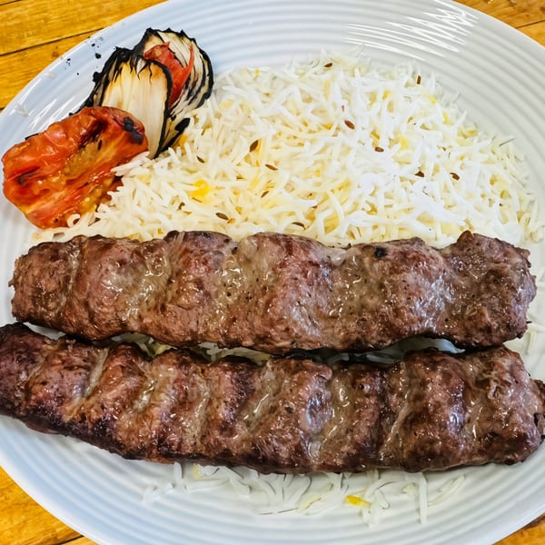 Two Afghan kabobs with white rice, grilled tomato, and onion on a white plate.