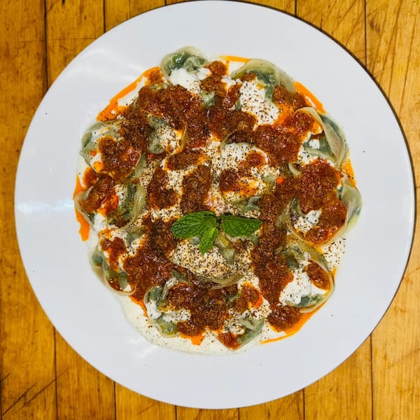Afghan Aushak dumplings with yogurt, meat sauce, and mint on a white plate.