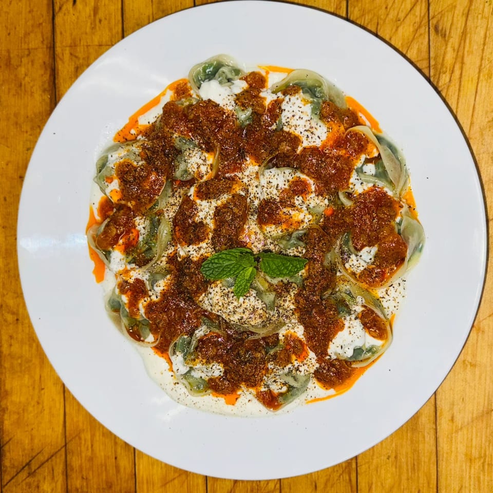 Afghan Aushak dumplings with yogurt, meat sauce, and mint on a white plate.